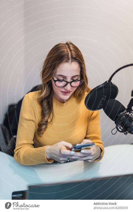 Content woman browsing smartphone at radio station text message work broadcast studio laptop microphone equipment device surfing modern sms cellphone mobile