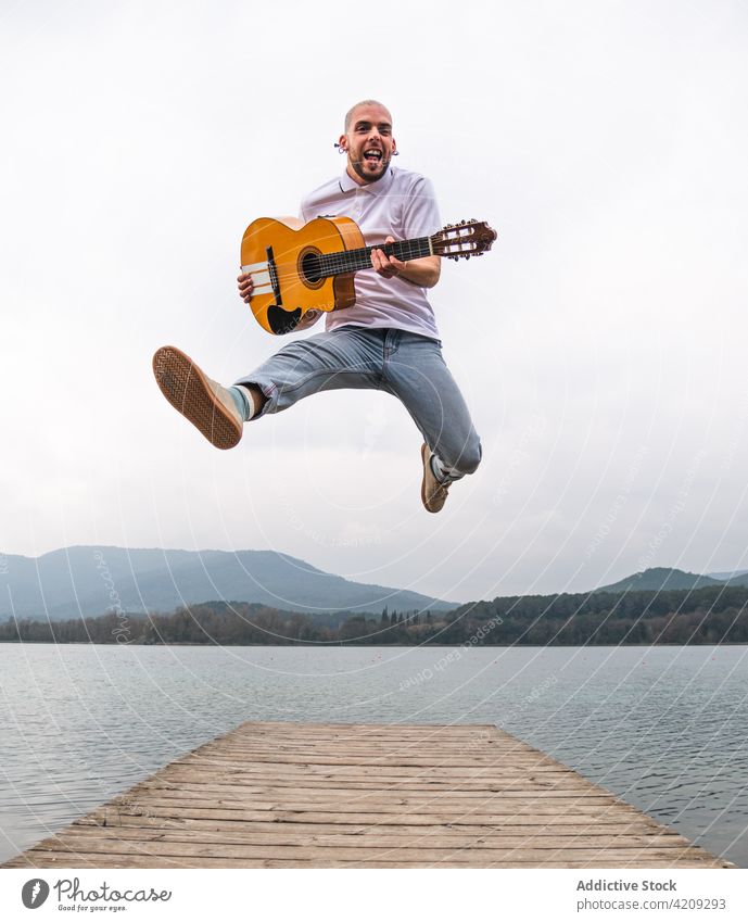 Man jumping with guitar on pier against river man freedom inspiration artist lake musician mountain guitarist nature shore male water bright pond beard day