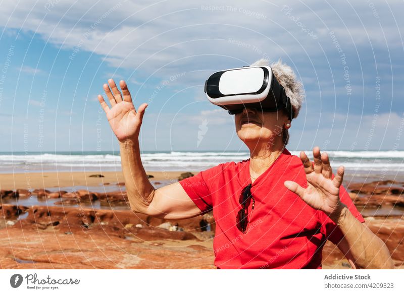 Unrecognizable senior tourist in VR headset on ocean beach virtual reality experience entertain technology modern seashore woman using gadget device