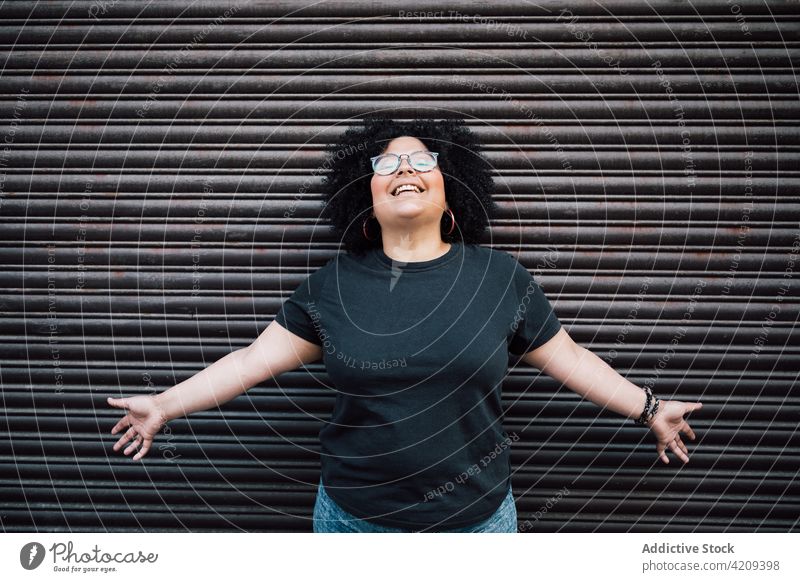 Happy plump woman with open arms against ribbed wall laugh sincere friendly eyewear happy afro charming portrait overweight enjoy smile pleasant cheerful glad