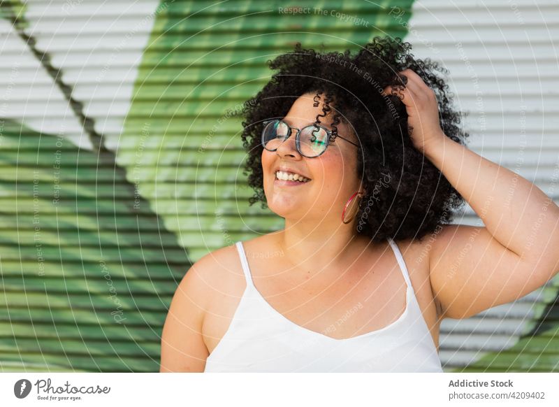 Happy plump woman in eyeglasses against ribbed wall touch hair laugh sincere friendly eyewear happy afro charming portrait overweight enjoy smile ornament