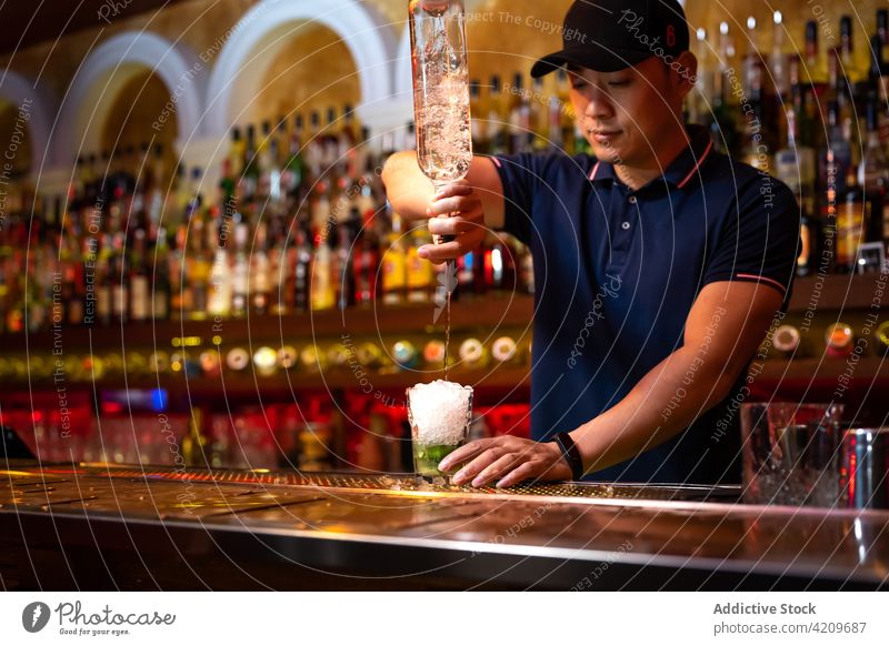 Young Asian bartender pouring rum in the glass while preparing a cocktail in the bar alcohol alcoholic aperitif barista barman beverage bottle business cap club