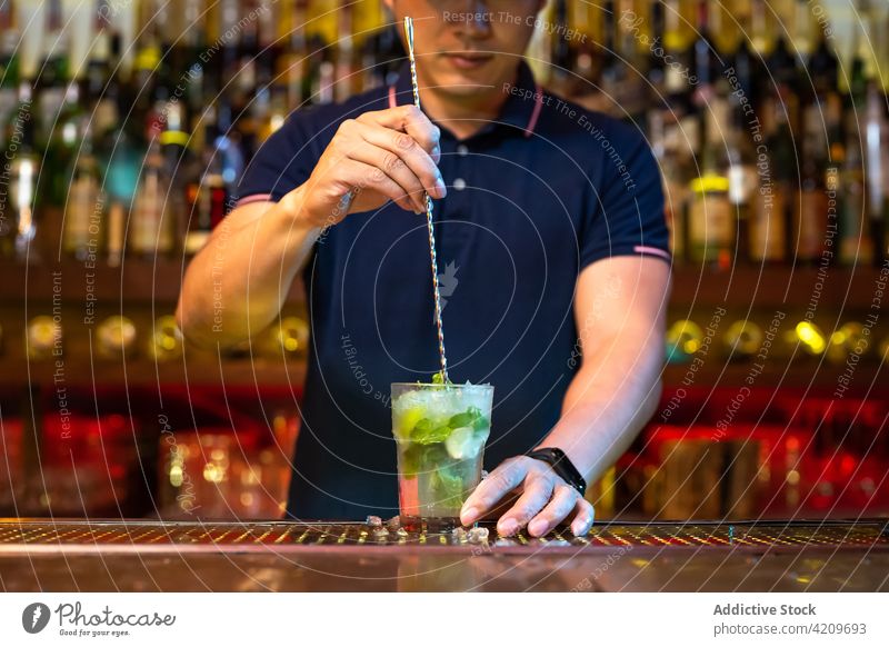 Unrecognizable bartender holding the glass and stirring mojito cocktail in the bar alcohol alcoholic aperitif barista barman beverage bottle business club