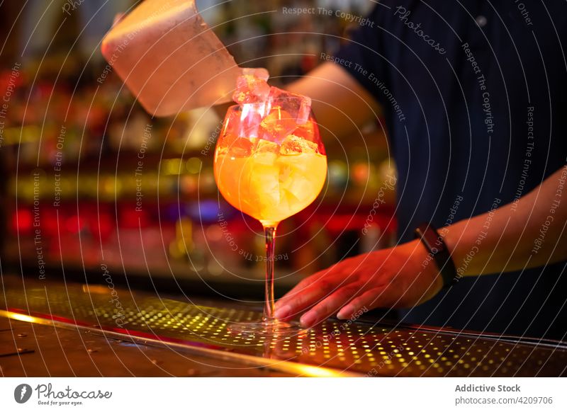 Unrecognizable bartender putting ice cubes into the glass while preparing a cocktail in the bar alcohol alcoholic aperitif barista barman beverage business club