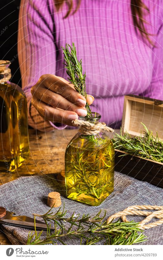 Unrecognizable lady putting rosemary in bottle with oil woman craft scent organic artisan small business herb chest rope textile table female twig fresh decor