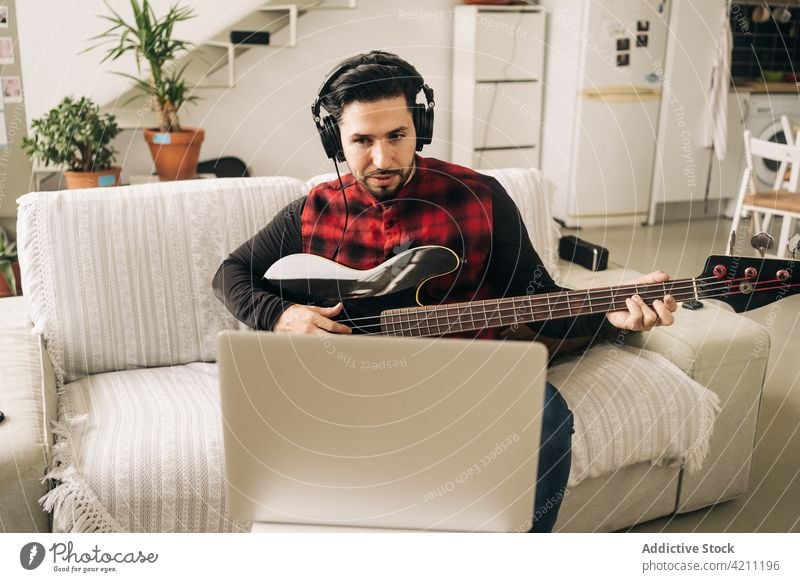 Bassist in headset playing guitar against laptop at home bassist lesson learn education study man using gadget device headphones guitarist video living room