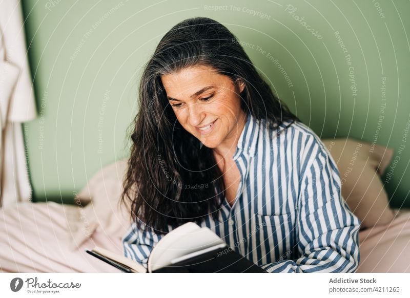 Pensive ethnic female sitting in bed and reading novel woman book pensive relax hobby tranquil literature peaceful interesting comfort mature hispanic casual