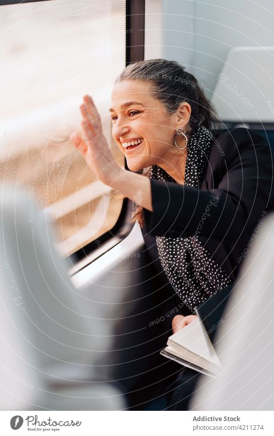 Smiling woman waving hand in train window wave hand greeting trip journey passenger wagon commute adventure mature middle age reflect scarf gesture gesticulate