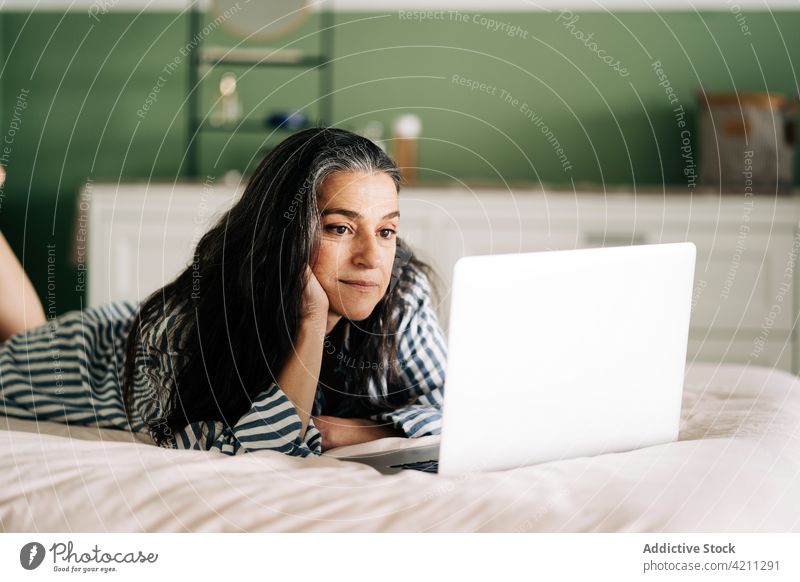 Ethnic female lying on bed and working remotely on netbook woman laptop freelance internet connection digital mature ethnic hispanic self employed home online