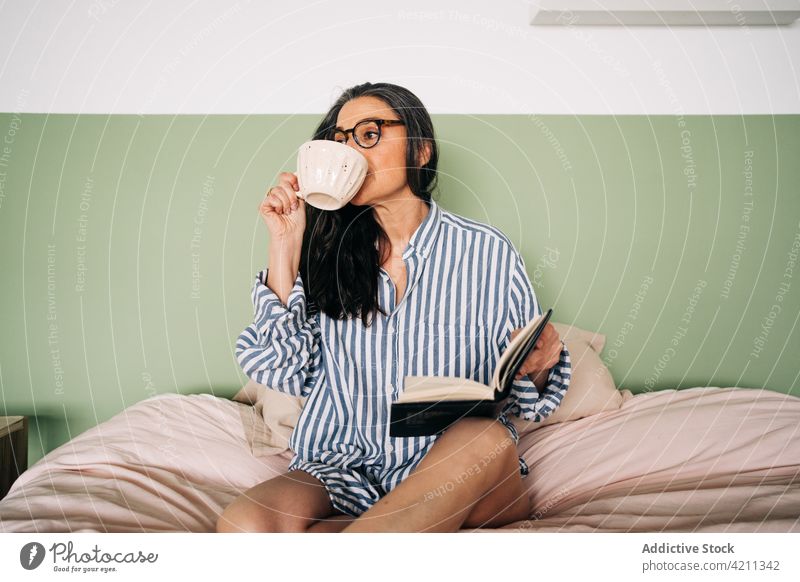 Woman with planner drinking coffee on bed woman cup notebook eyeglasses peaceful leisure female stripe shirt home bedroom soft tranquil smart comfort lady