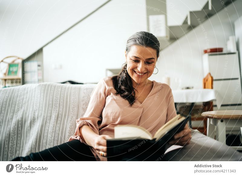 Concentrated woman reading book on couch smile sofa apartment happy domestic hobby bookworm glad living room female home casual concentrate delight comfort flat