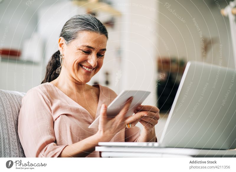 Smiling mature woman looking at photo near laptop admire examine middle age sofa room home netbook kitchen female gadget device enjoy apartment computer casual