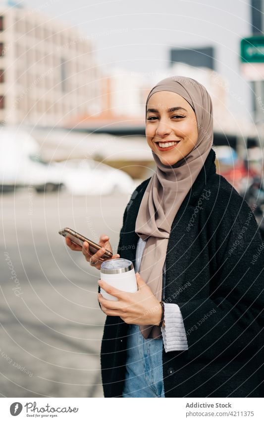 Cheerful stylish Muslim woman browsing smartphone in city message takeaway drink enjoy walk hijab surfing female ethnic muslim headscarf internet trendy style