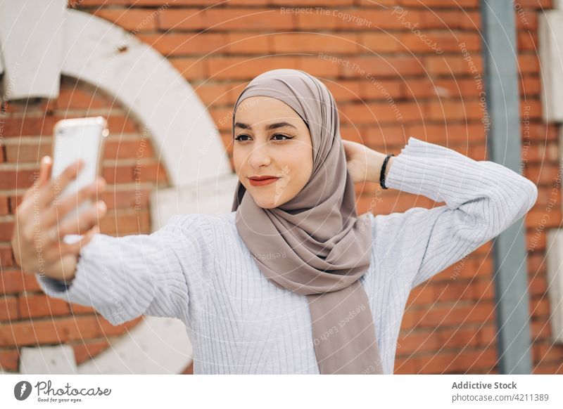Charming ethnic woman in headscarf taking selfie in city smartphone self portrait hijab cheerful entertain charming female muslim tradition street gadget young