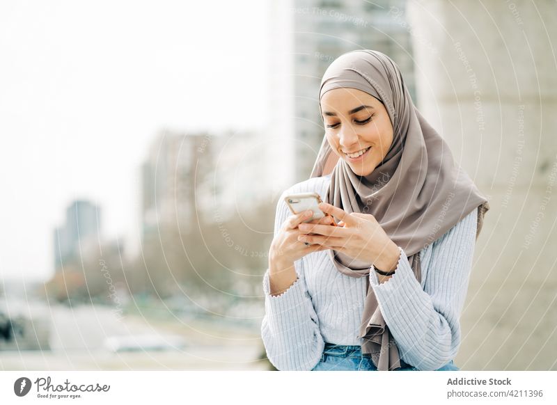 Muslim woman using smartphone on street browsing city message social media young hijab tradition female ethnic muslim mobile connection online border stone sit