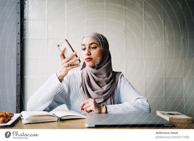 Muslim female entrepreneur recording voice message on smartphone woman audio work freelance cafe using ethnic muslim table remote gadget device cellphone mobile