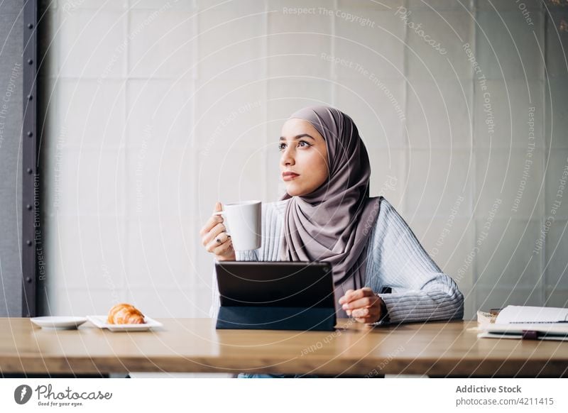 Thoughtful Muslim woman with drink and tablet in cafe freelance work thoughtful cup pensive hijab female ethnic muslim project sit entrepreneur beverage lady