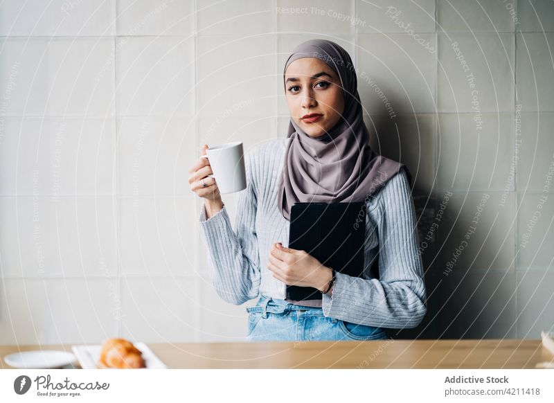 Portrait of Muslim woman with drink and tablet in cafe freelance work thoughtful cup pensive hijab female ethnic muslim project entrepreneur beverage lady