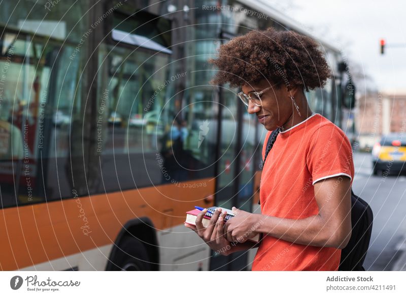 Smiling young African American guy standing at roadside before studies man smile street city content trendy bus personality cool confident urban male