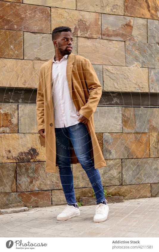 Stylish black man standing on street and looking away style coat city trendy outfit handsome apparel urban male ethnic african american stone wall building