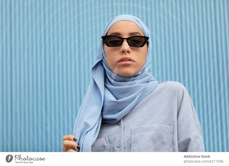 Trendy Muslim woman in sunglasses on blue background fashion style headscarf contemplate individuality accessory islam portrait casual cool modern color dreamy