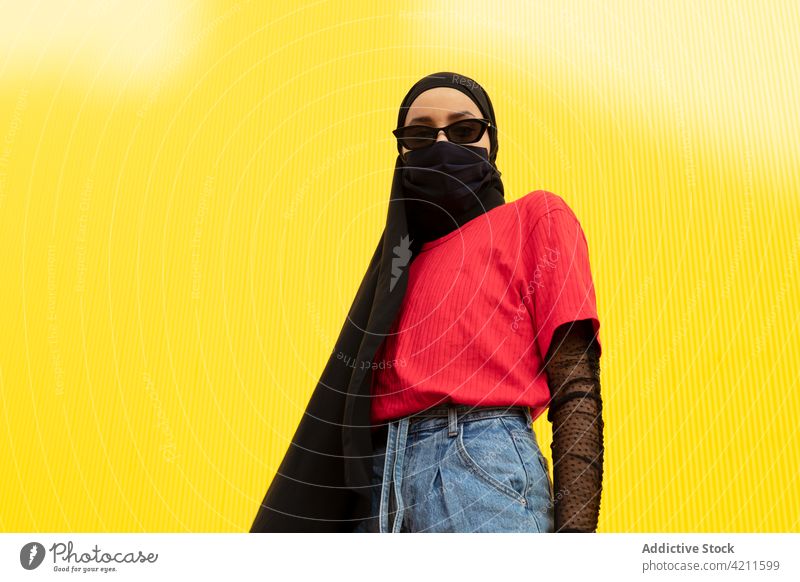 Trendy Muslim woman in sunglasses on yellow background fashion style individuality headscarf cool mask portrait colorful covid 19 cloth health care protect