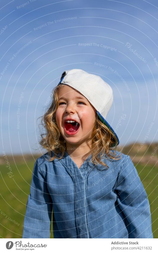 Excited girl in cap in nature summer meadow excited blue sky mouth opened style blond kid happy cheerful pleasure glad positive carefree joy holiday relax cute