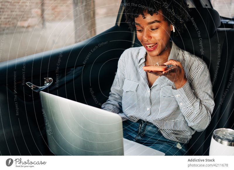 Young black woman using smartphone and laptop in car happy smile audio ride netbook taxi work commute young job remote african american computer mobile lady