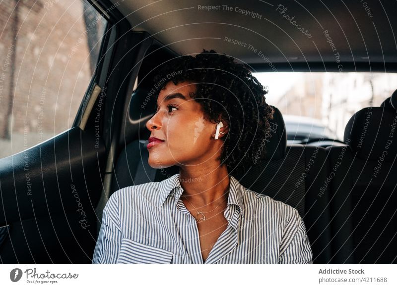Young black female passenger resting on backseat in car woman listen music tws true wireless earbuds happy smile commute chill taxi relax modern young