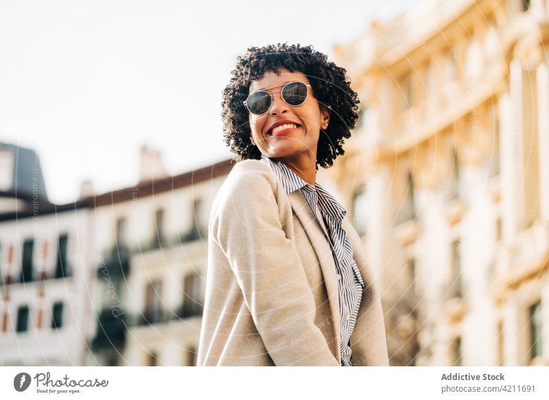 Cheerful black woman in trendy sunglasses smiling on street cheerful town smile positive happy coat urban fashion outfit city female young glad appearance