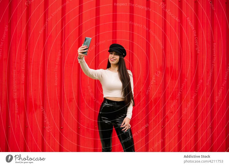 Smiling stylish businesswoman taking selfie in city cheerful entrepreneur style trendy memory self portrait smartphone female red wall smile street modern happy