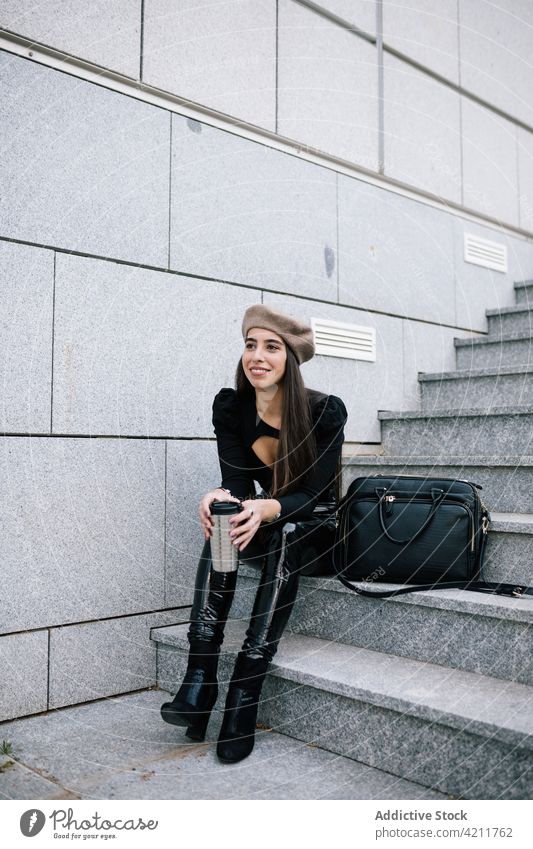 Smiling businesswoman sitting on stairs with takeaway drink city to go street enjoy style trendy female beret hat entrepreneur smile beverage outfit urban