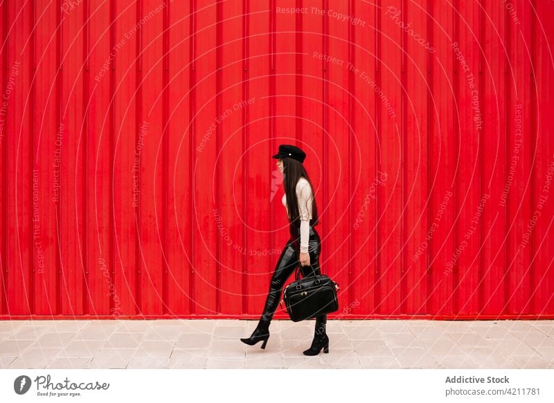 Stylish businesswoman walking along street in city entrepreneur style well dressed trendy sidewalk urban female outfit red wall confident charming cloth modern