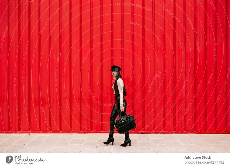 Stylish businesswoman walking along street in city entrepreneur style well dressed trendy sidewalk urban female outfit red wall confident charming cloth modern