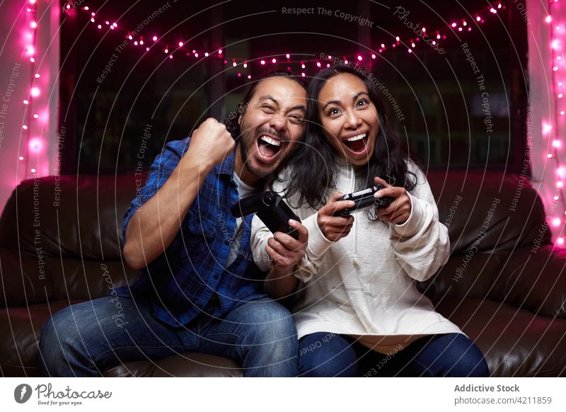 Delighted ethnic couple playing video game together delight videogame excited couch joy pad having fun entertain laugh gamepad free time device pastime