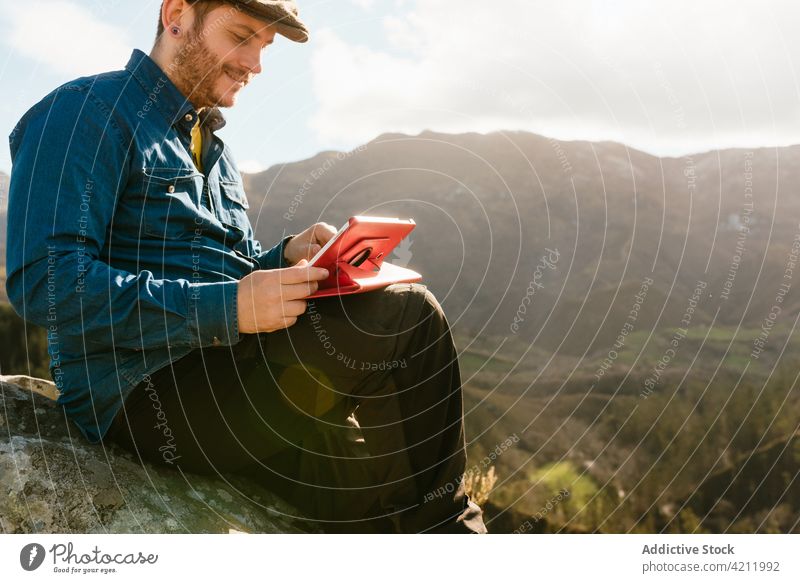 Traveler with tablet sitting on rocky hill in highlands traveler mountain man admire enjoy viewpoint freedom male vacation explore nature scenery adventure