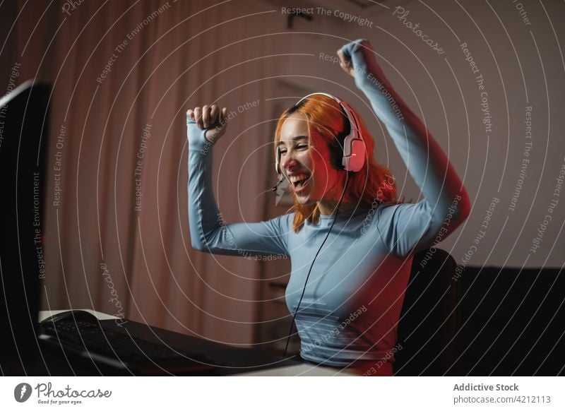 Cheerful gamer celebrating victory in videogame celebrate woman win winner triumph excited success female headphones happy home device gadget using listen glad