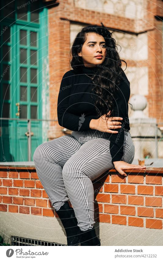 Curvy female in stylish clothes near brick building woman coat plus size style trendy fashion curve model determine city street sit border confident outfit