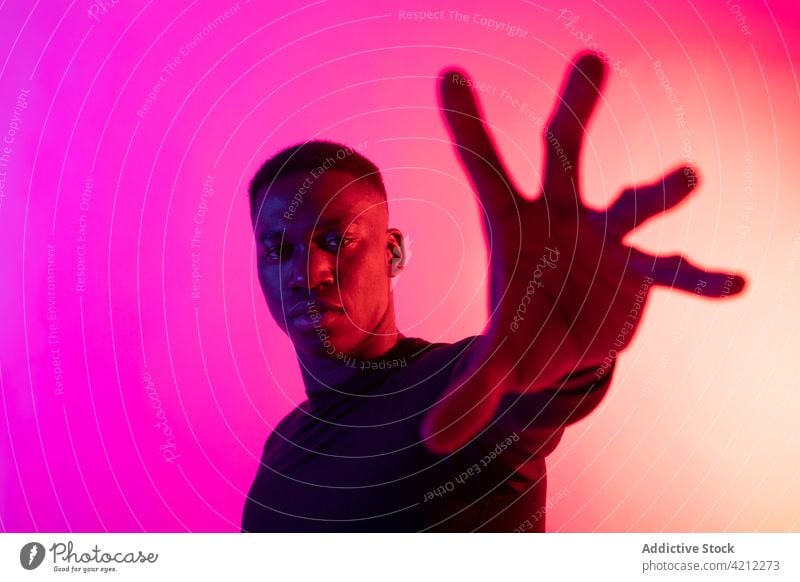 Confident African American man outstretching hand to camera in studio confident neon reach out stop studio shot determine colorful alone concentrate serious