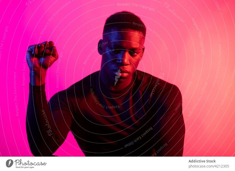 Serious African American male in neon studio man serious unemotional studio shot fist sportive athlete personality alone portrait confident glow