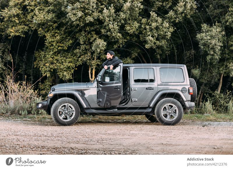 Adventurer leaning on the door of an off-road car man adventure jeep vehicle transportation 4wd traveler adventurer copy space 4x4 green journey nature mountain