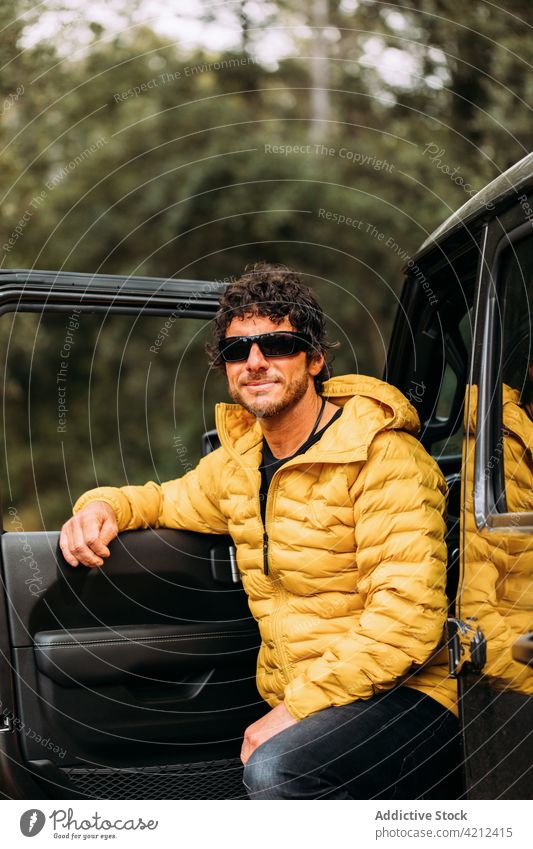 Adventurer in sunglasses and yellow jacket next to his off-road car man happy nature vacation freedom person journey travel transportation lifestyle outdoor