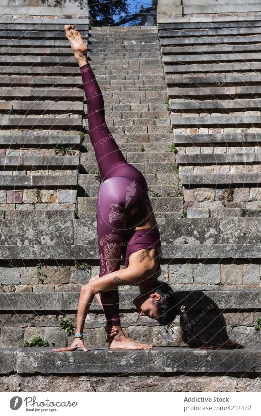 Flexible woman balancing in split while doing yoga balance practice pose urdhva prasarita eka padasana flexible stretch female bend forward bend stone stair