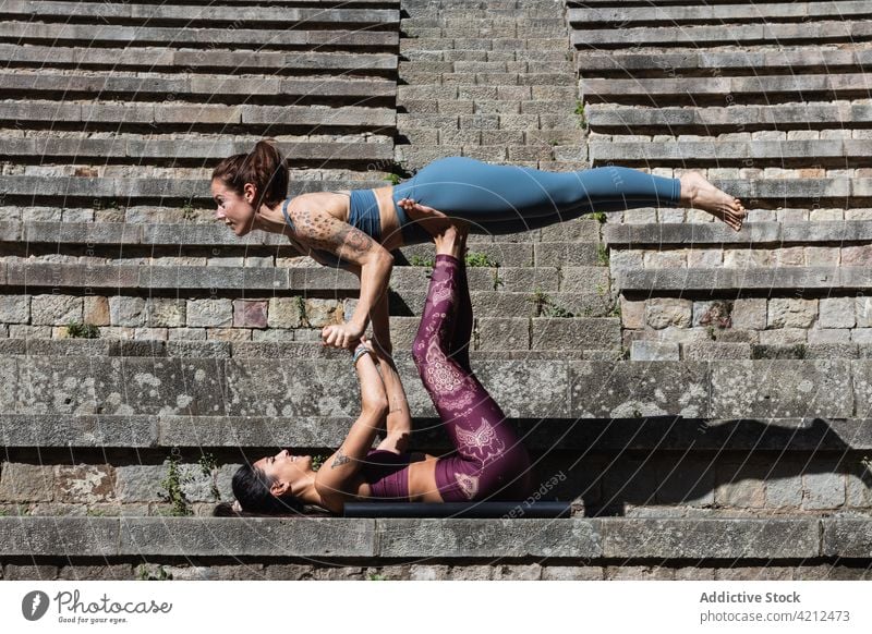 Fit women doing acro yoga together on mat practice acrobatic support balance flexible asana female wellbeing vitality harmony stone healthy stretch pose