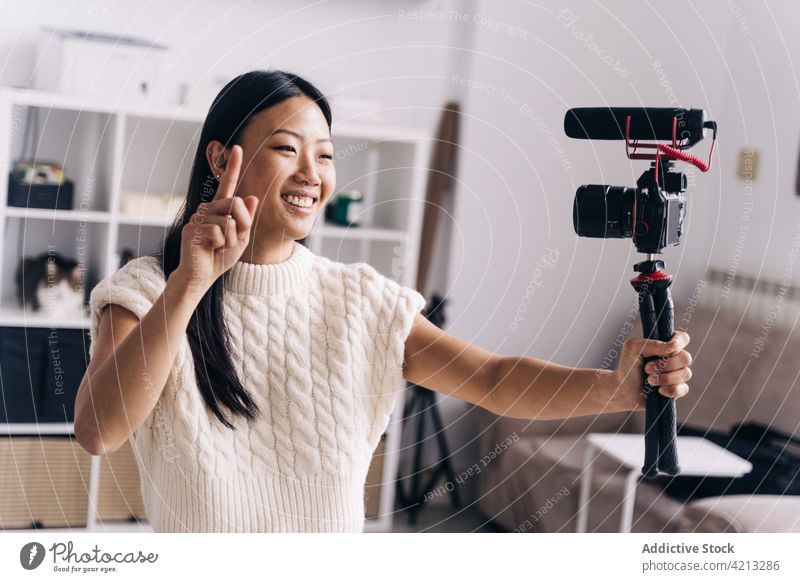 Cheerful Asian blogger recording video on photo camera on sofa vlogger cheerful social media woman using device living room couch glad friendly stand house home