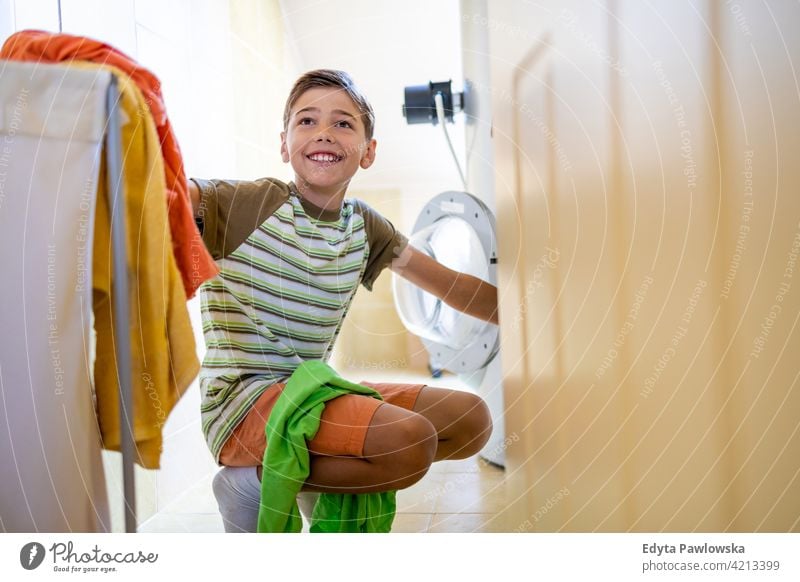 Boy loading washing machine at home washer laundry clothes bathroom housework chores helping learning family people child son boy kid kids children lifestyle