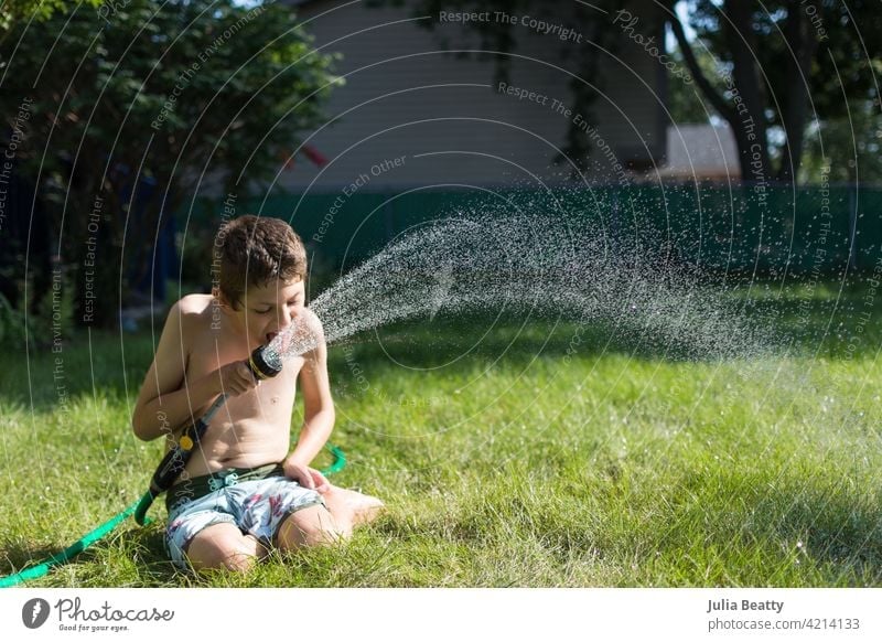 Young boy with Autism playing with garden hose in his backyard; summer time in the Midwest USA spray drink sensory sensory seeker autism special needs utility