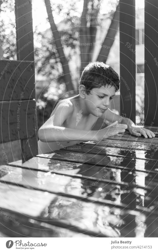 Boy climbing into wooden playset to play in a puddle of water; sensory play for child with Autism water play Puddle playground playhouse hose garden hose splash