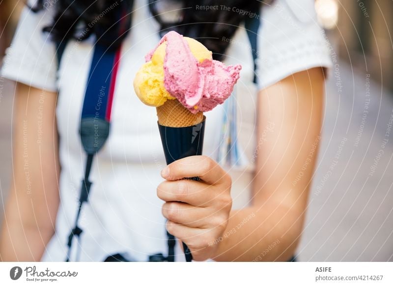 Hand of a tourist woman holding a big two flavored ice cream cone hand scoop waffle street people outdoors travel summer mango fruit strawberry cold delicious