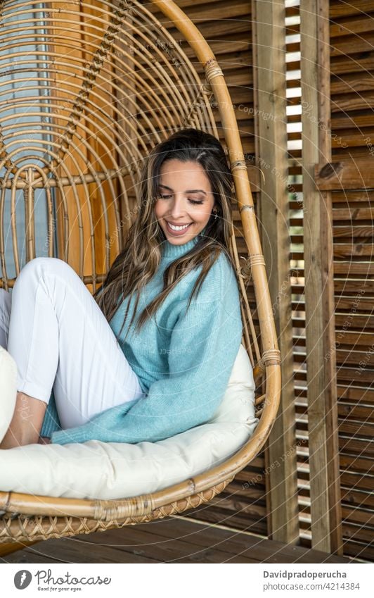 Cheerful woman resting in wicker hanging chair chill natural wooden happy style enjoy furniture rattan cushion comfort home smile cheerful design charming